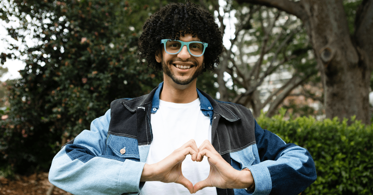 man smiles while using his hands to display a heart over his chest