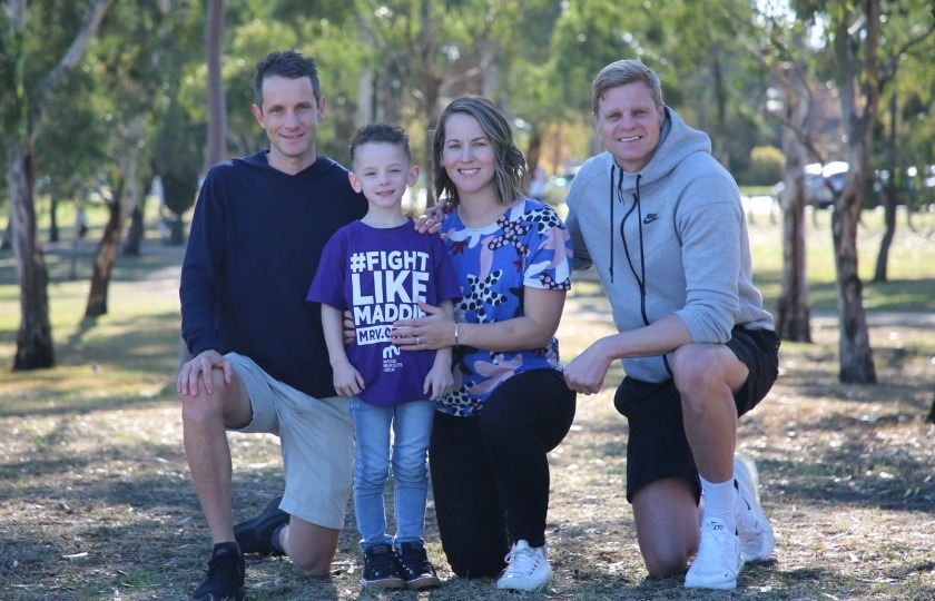 A family of four in a park looking at the camera. The little boy has a tshirt on saying "Fight like Maddie"